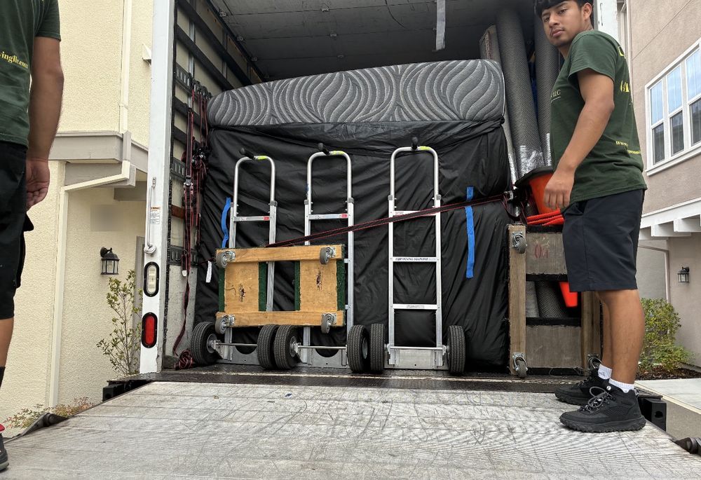 A crew member beside an open moving truck with a padded mattress, dollies and hand trucks strapped in and ready at the liftgate
